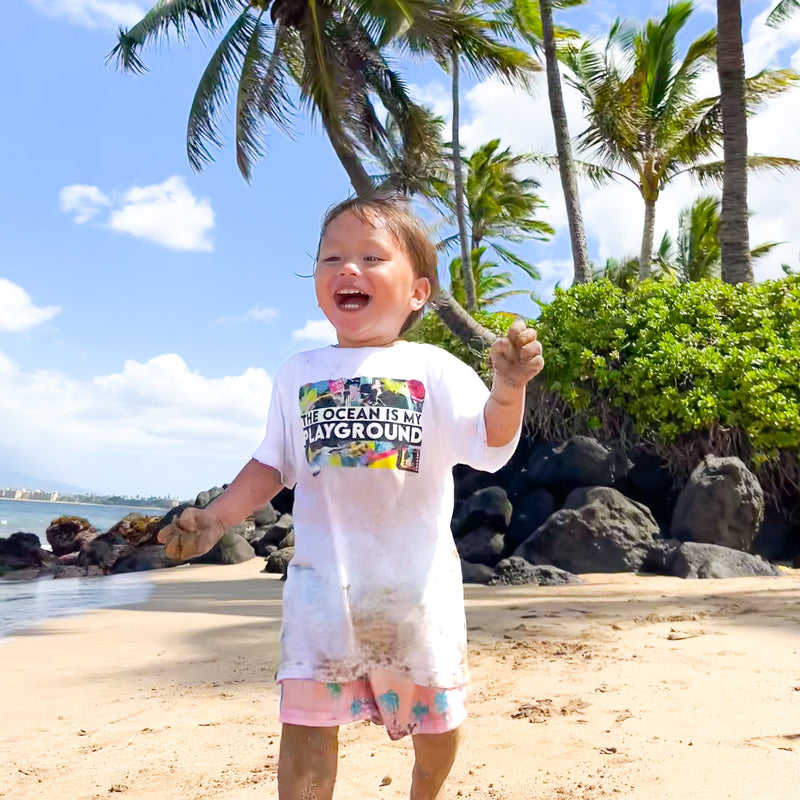 Child on a beach with palm trees and rocks in the background